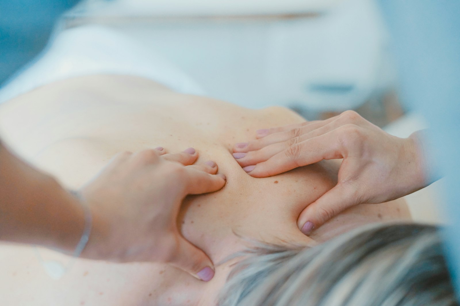 A quiet corner of a massage clinic with a wooden bench, folded robe, aromatherapy diffuser, and a framed anatomical illustration